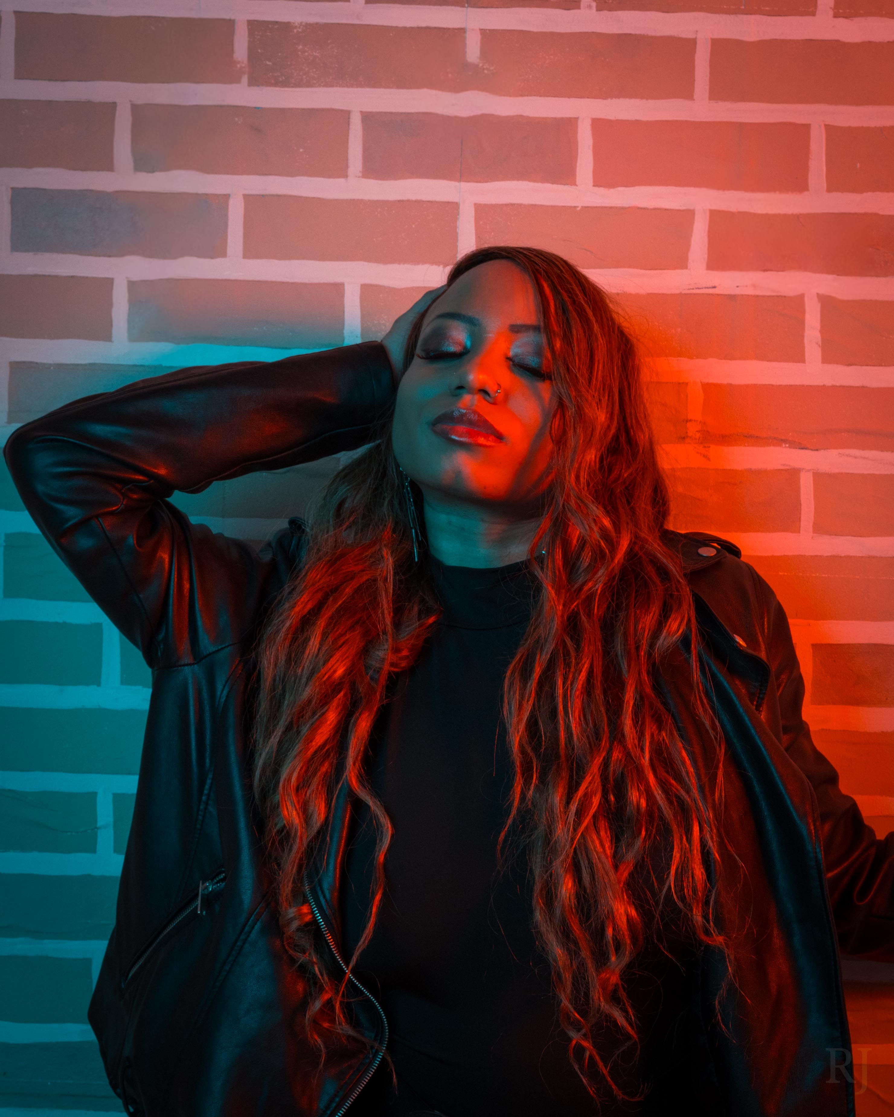 Stylish woman with long hair against brick wall with colorful lighting.