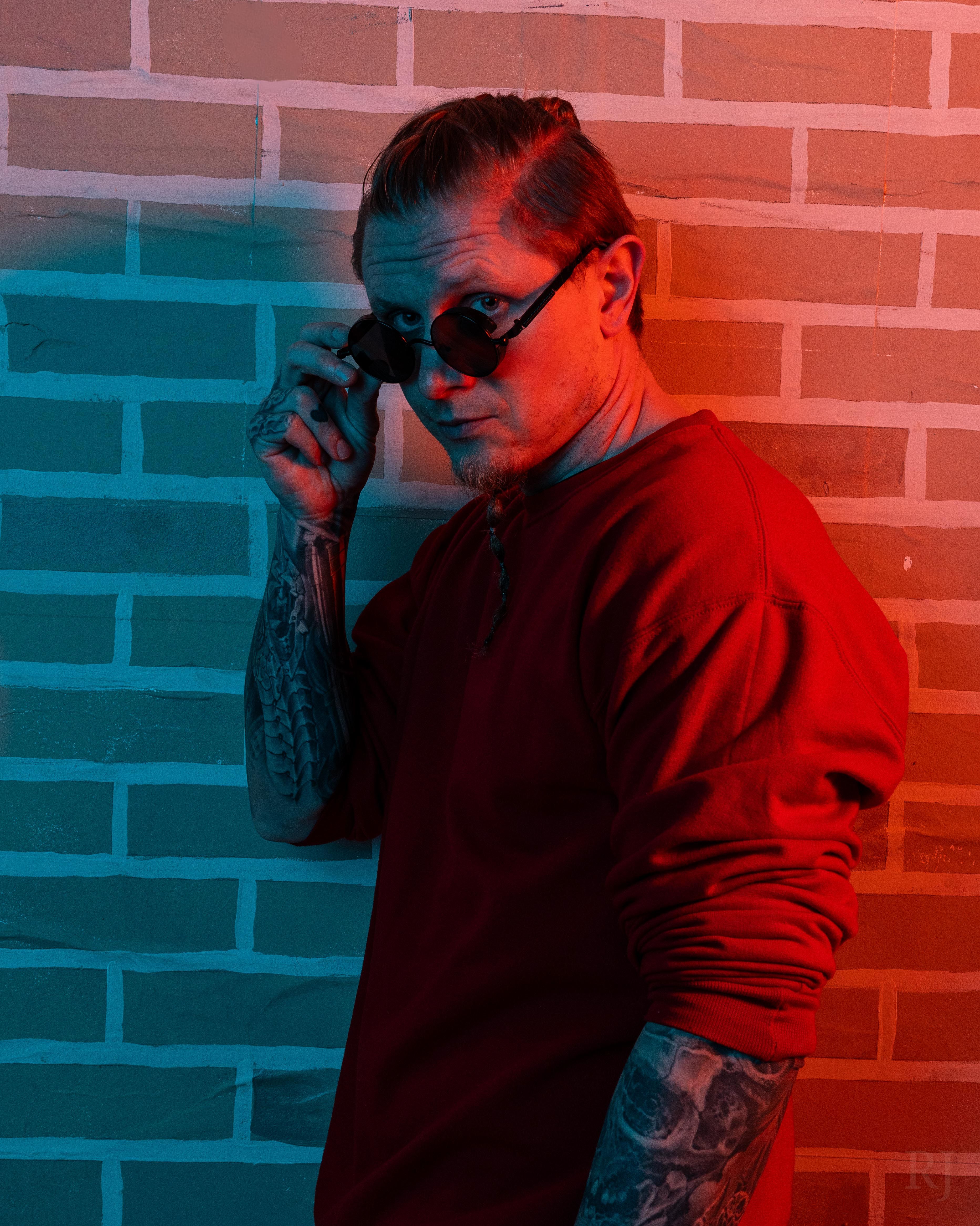 Confident man in sunglasses poses with dramatic red and blue lighting.