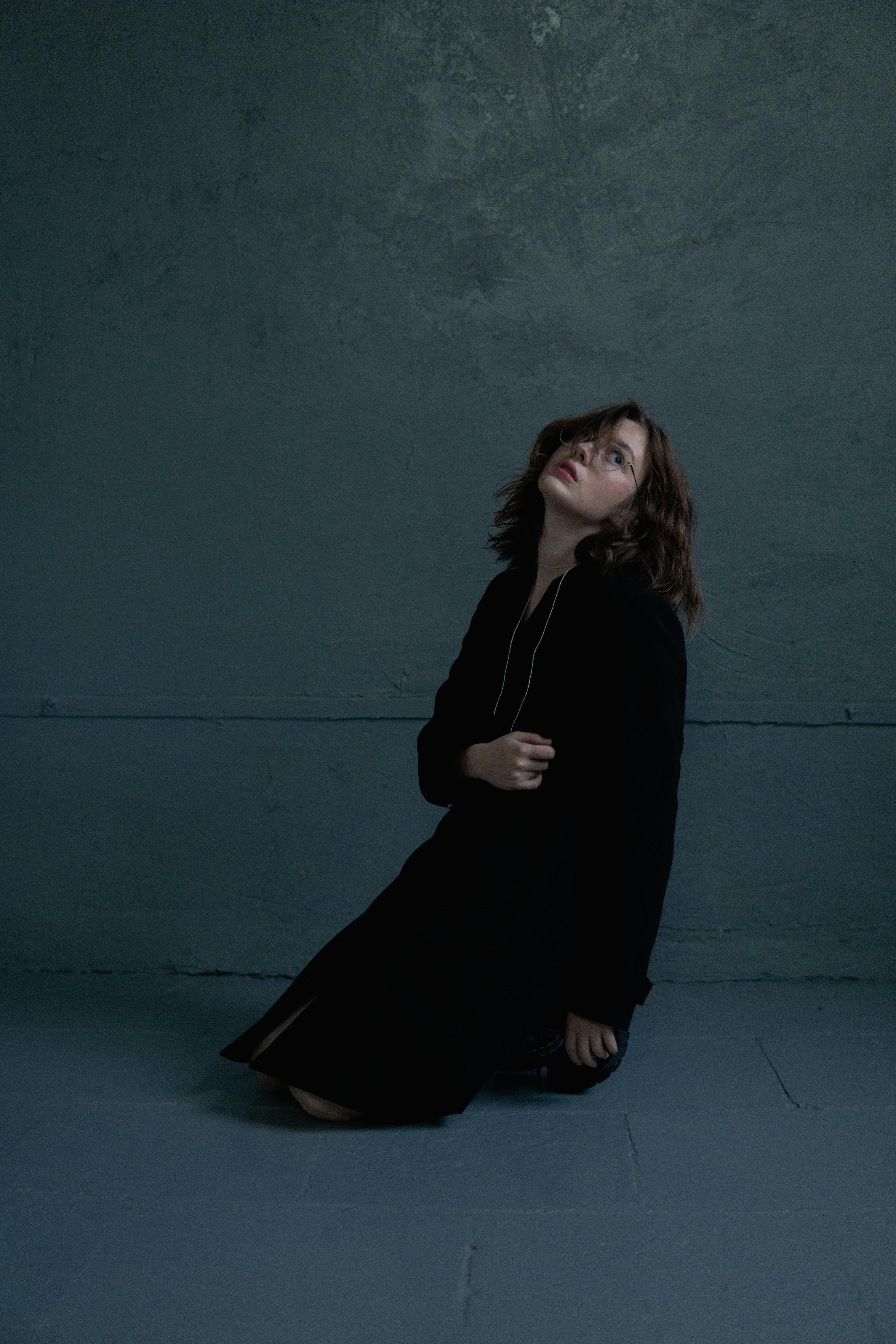 Dramatic portrait of a woman in a dark, minimalist setting wearing a black outfit.