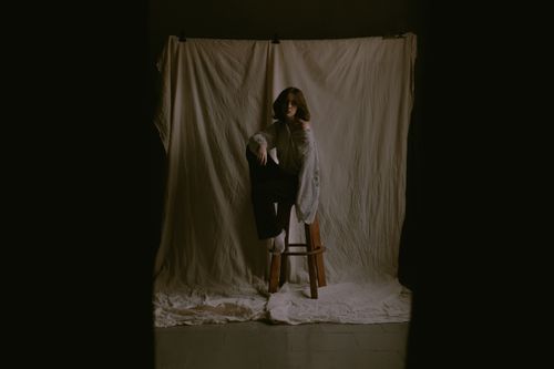 Free A woman in knitwear poses on a stool in a dark studio environment. Stock Photo