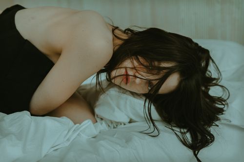 Free Moody portrait of a woman with long dark hair lying on a bed, conveying emotion. Stock Photo