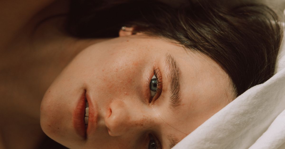 Captivating portrait of a young woman with freckles lying on a bed, enveloped in soft light.
