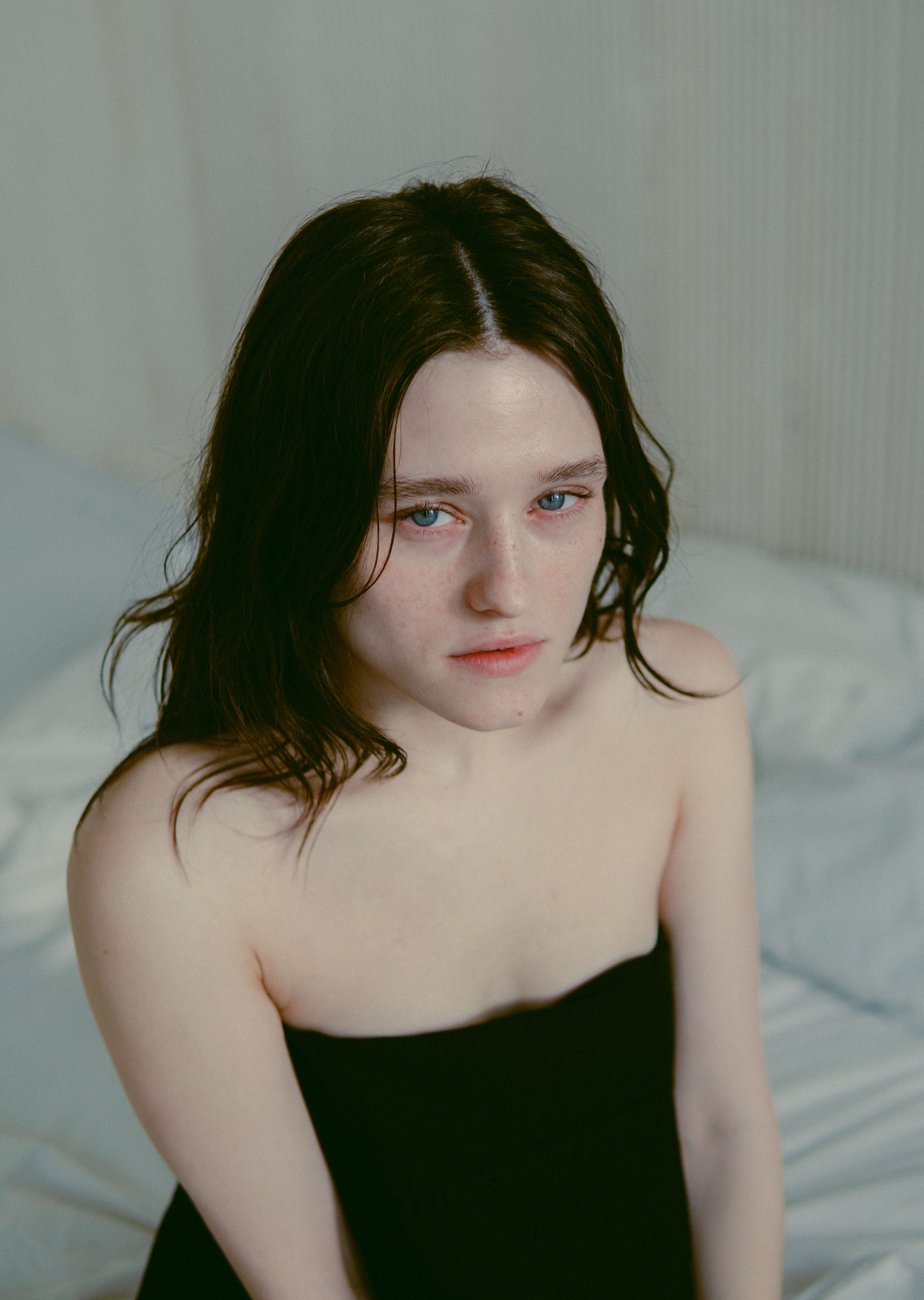 Portrait of a young woman with tired expression, posing in a strapless dress indoors.