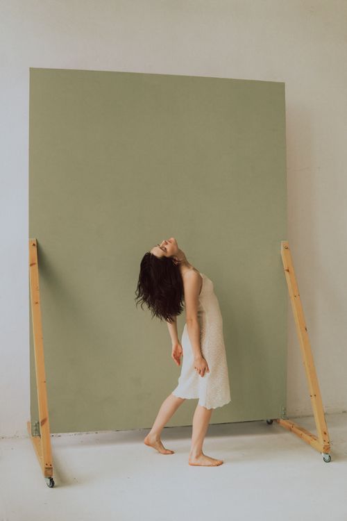 Free Brunette woman in a white dress poses artistically against a green backdrop in a studio setting. Stock Photo