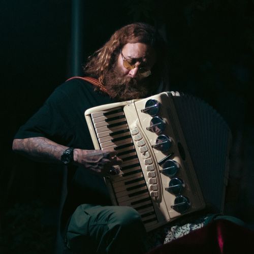 Free A bearded musician plays an accordion outdoors, creating a soulful performance. Stock Photo