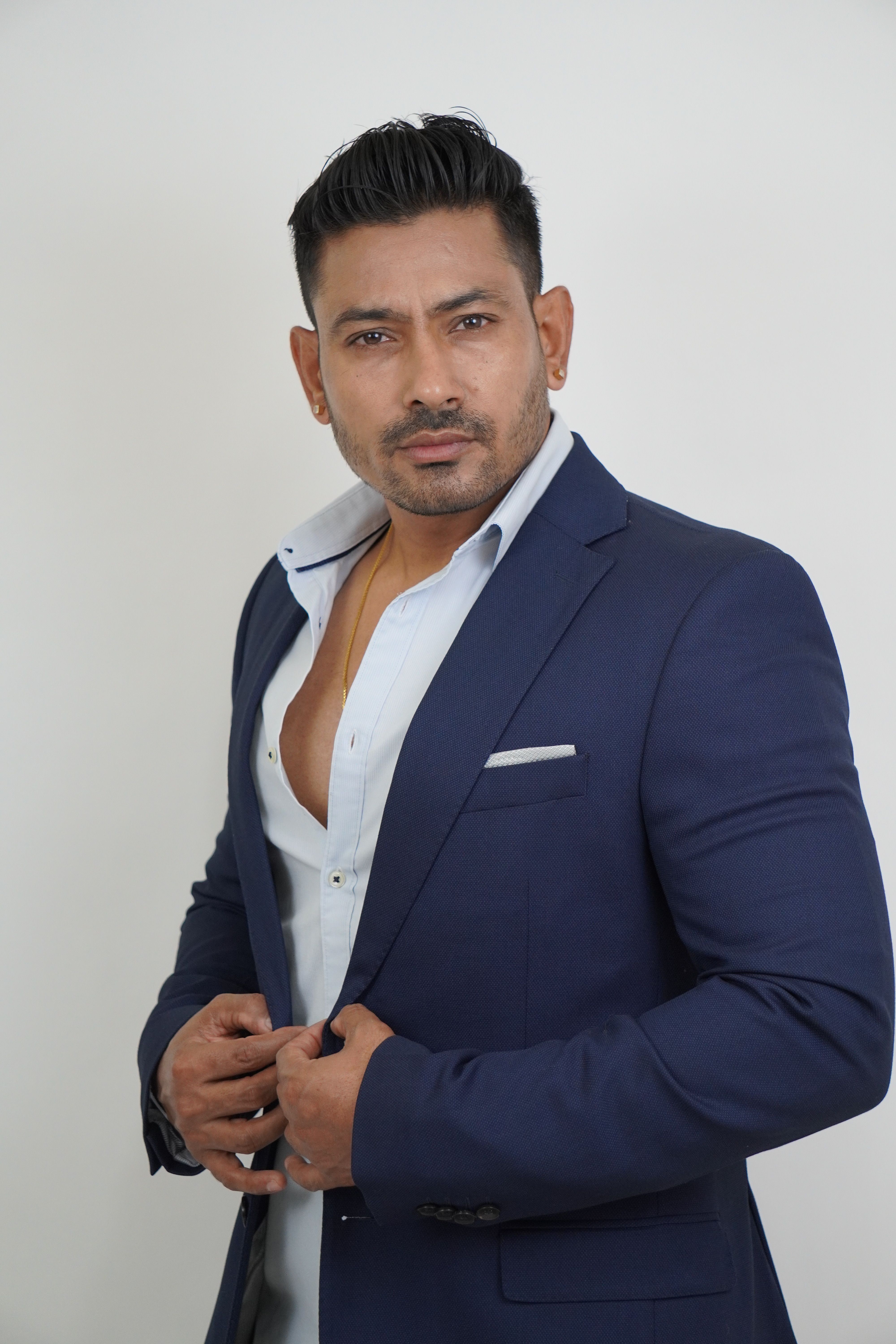 Fashionable male model in a navy suit with a confident pose on white backdrop.