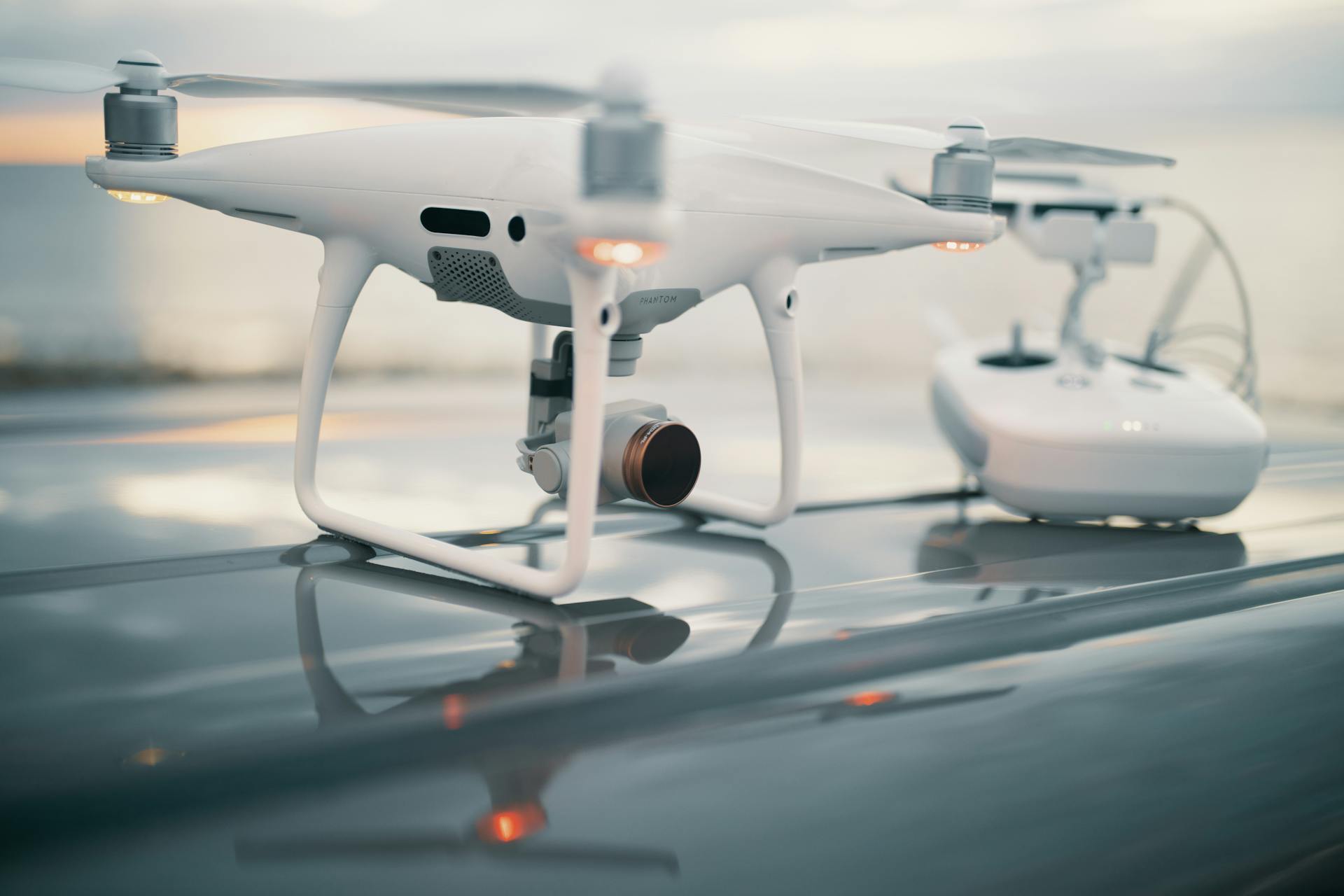 A close-up view of a sleek drone with its controller on a reflective surface during sunset.