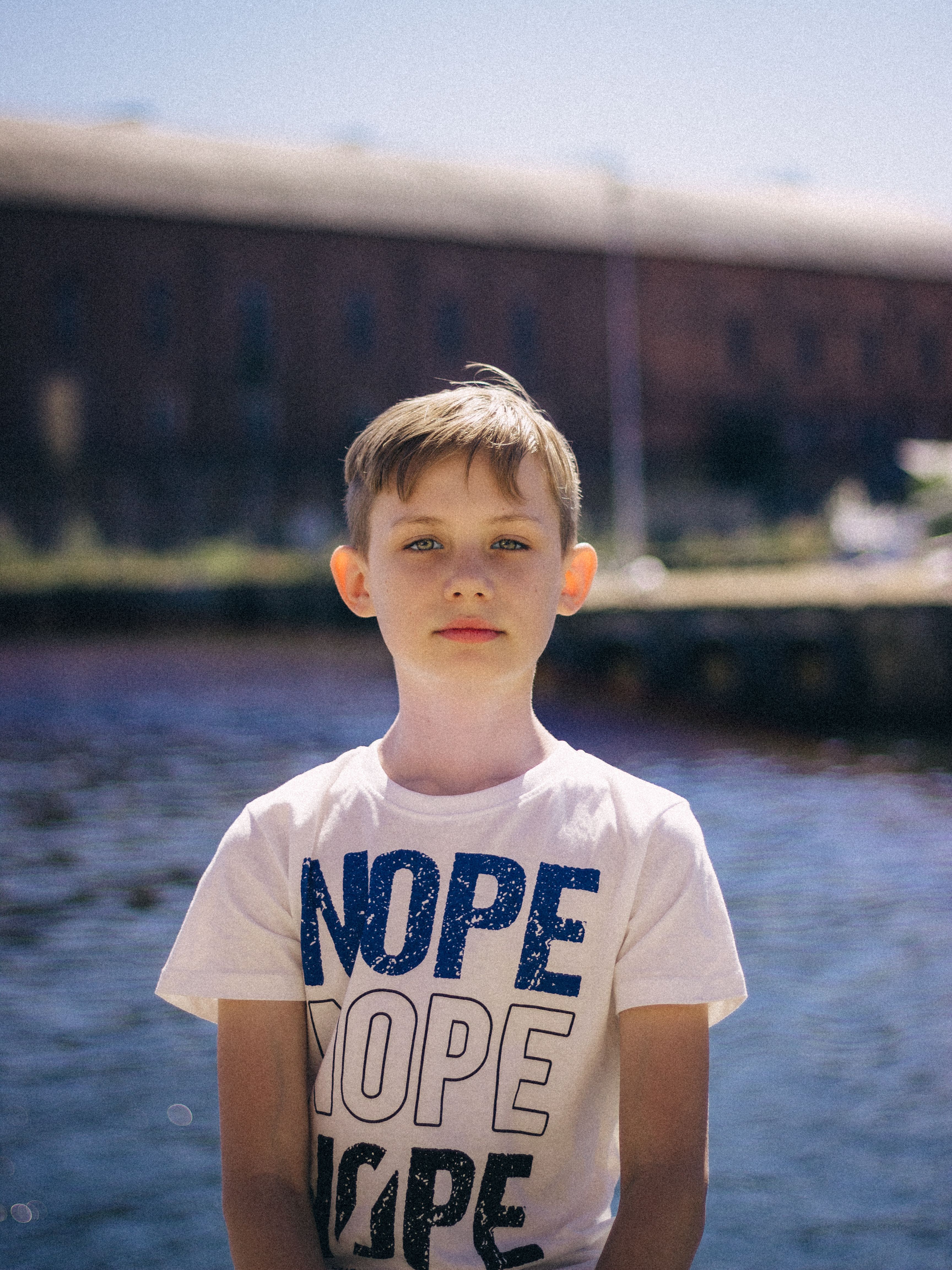 Young boy in a white t-shirt standing by a lakeside in Słupsk, Poland, on a sunny day.