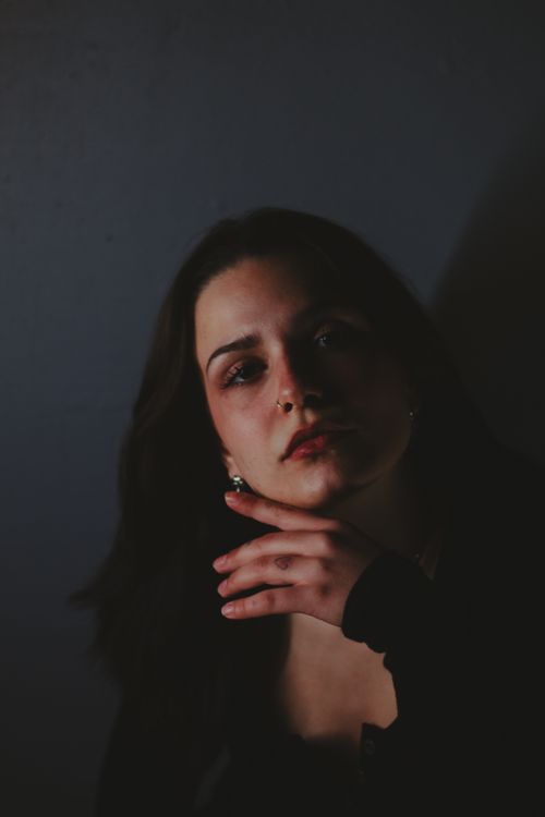 Free A pensive woman with hand on chin captured in dramatic lighting. Stock Photo
