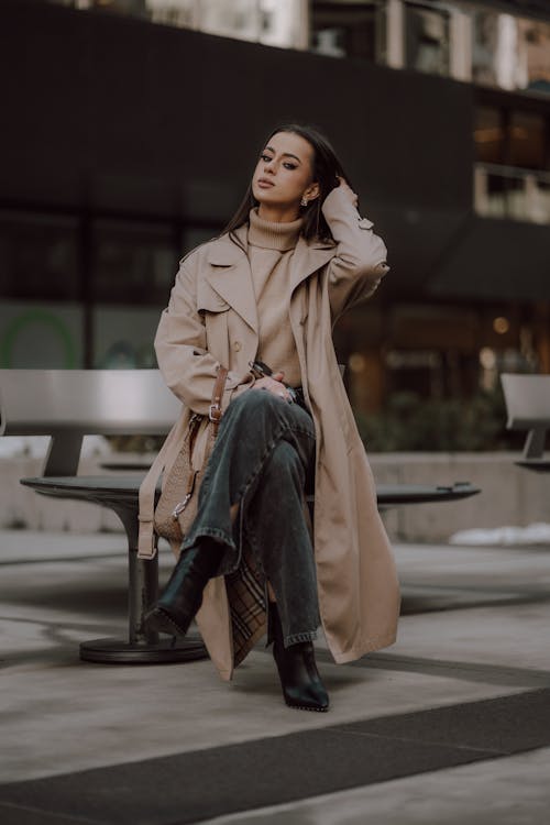 Woman in Trench Sitting on Bench and Fixing Hair