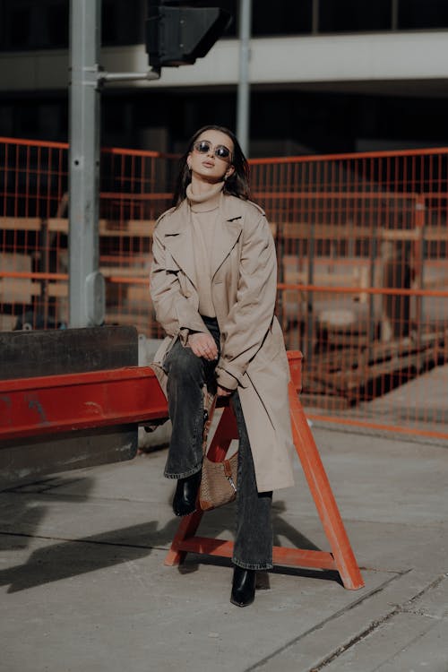 A woman in a trench coat and sunglasses sitting on a chair