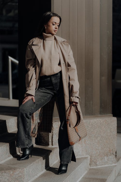 A woman in a trench coat and jeans is standing on steps