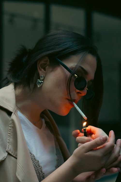 Free Fashionable woman using a lighter to ignite a cigarette in a moody outdoor setting. Stock Photo