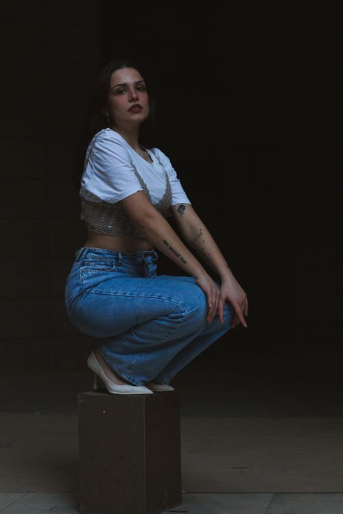 Free Fashionable young woman squatting in jeans and a crop top, showcasing urban style with tattoos. Stock Photo