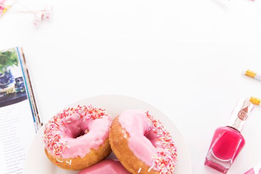 Delicious pink frosted donuts with sprinkles on a plate, paired with nail polish.