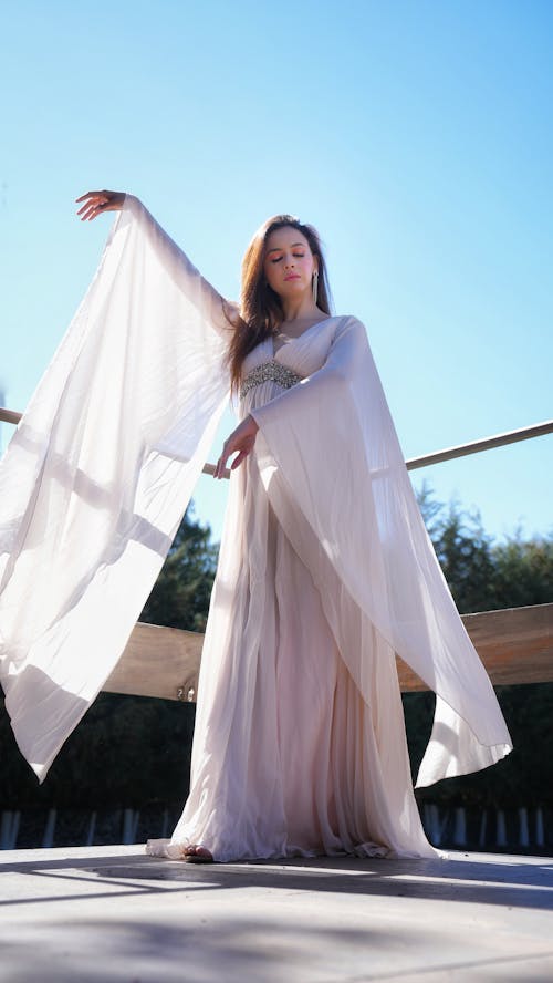 A woman in a long white dress is posing