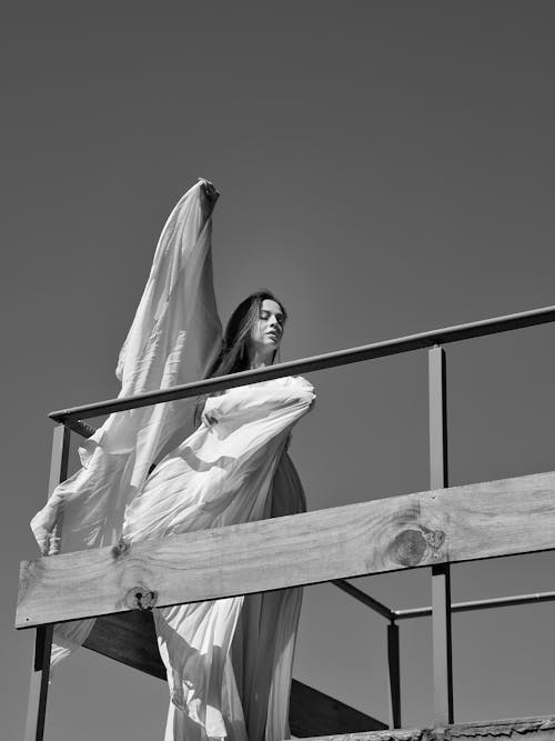 A woman in a white dress is standing on a wooden railing