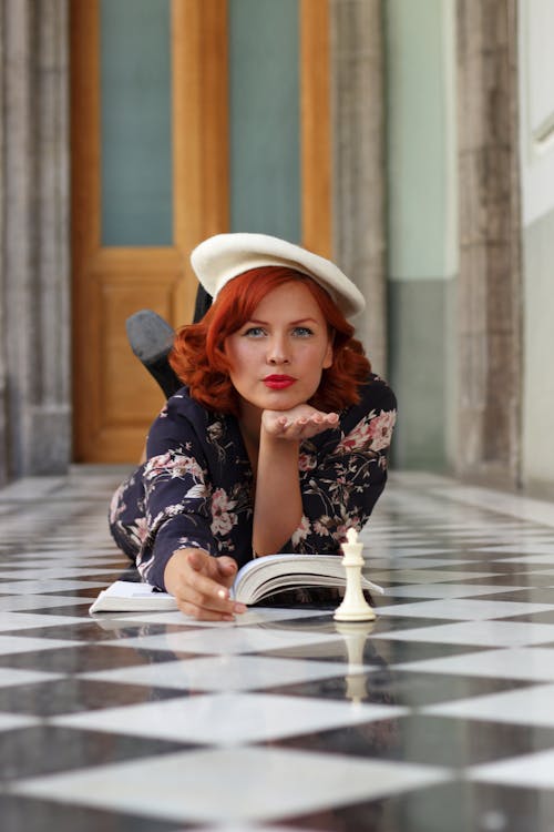 A woman with red hair and a hat laying on the floor