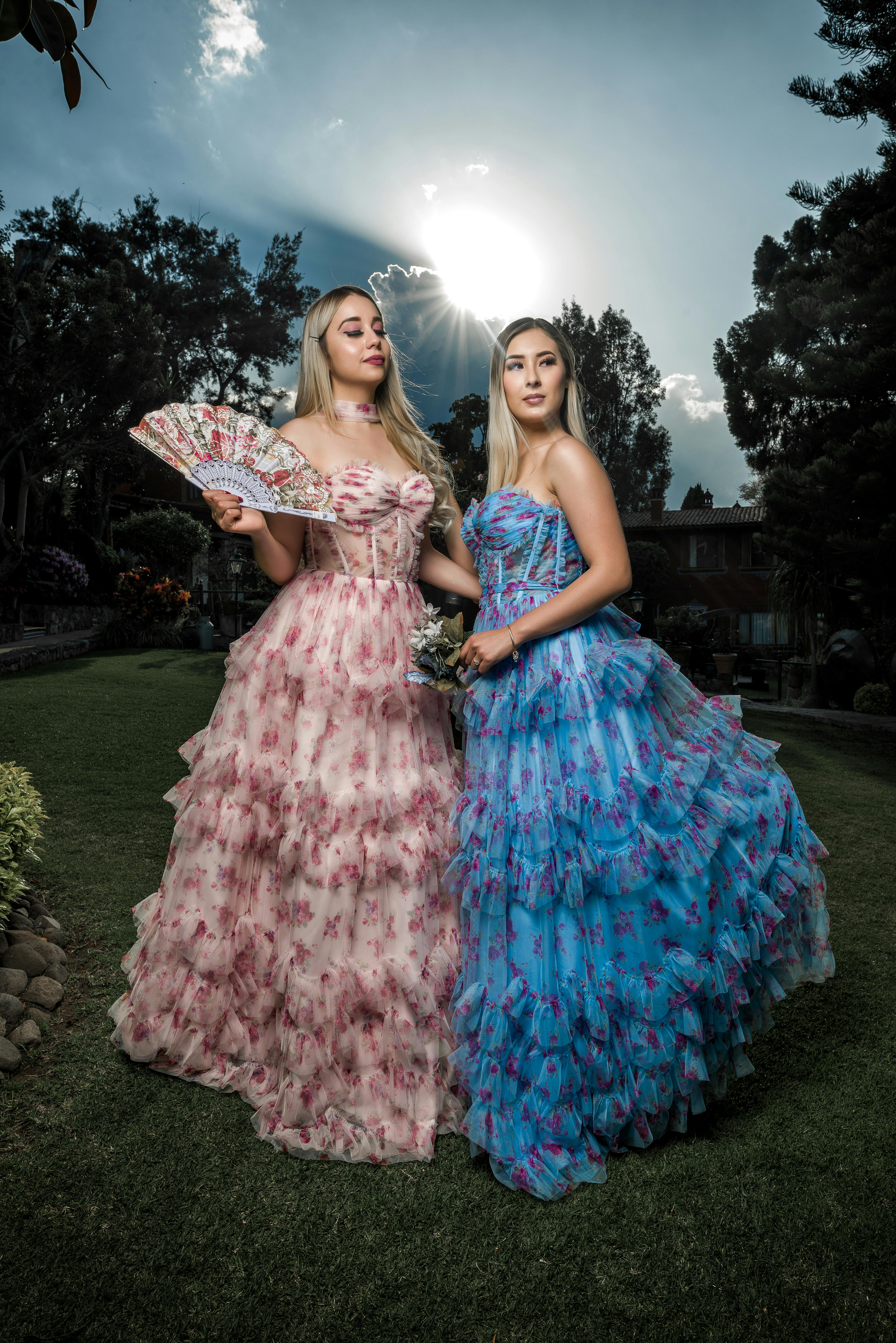 Two women in floral dresses posing elegantly outdoors with a sunset backdrop.