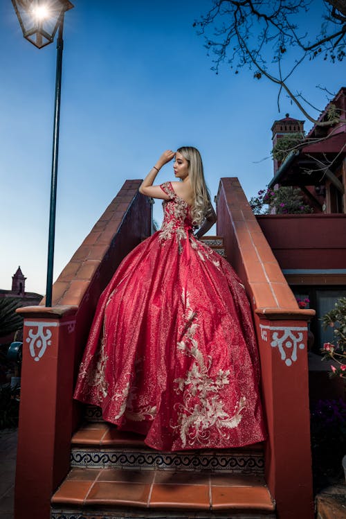 A beautiful blonde woman in a red dress is standing on some stairs