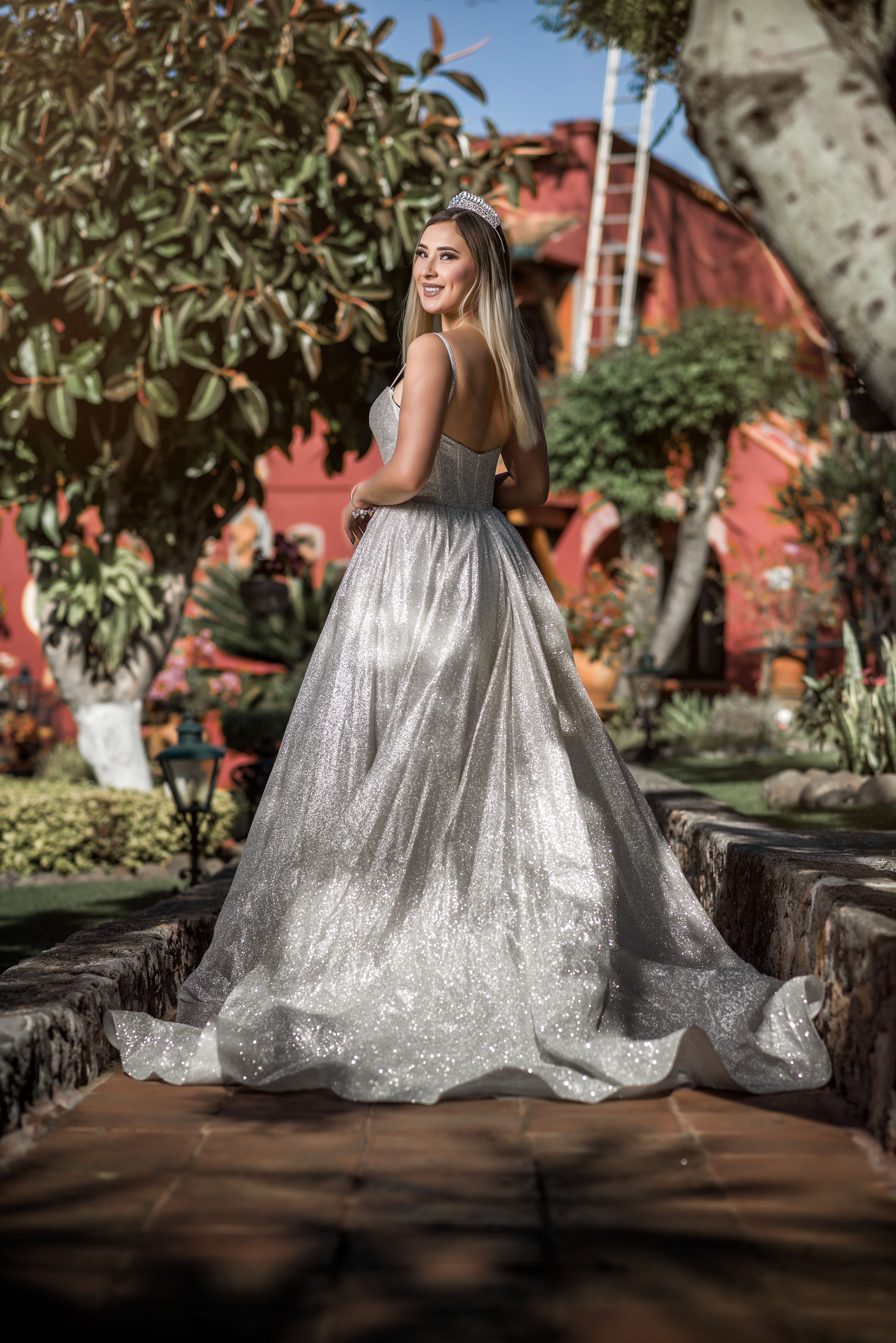 A bride in a stunning shimmering gown poses elegantly in a beautiful garden setting.