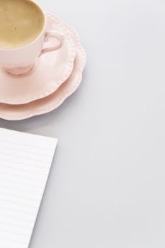 Minimalist photo of a pink coffee cup on saucer with a notepad, perfect for lifestyle themes.