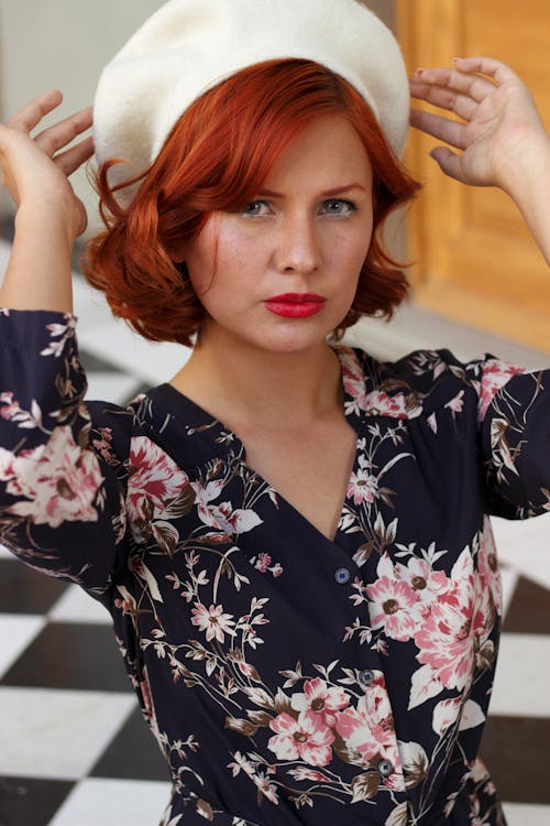 A woman with red hair wearing a hat and floral dress