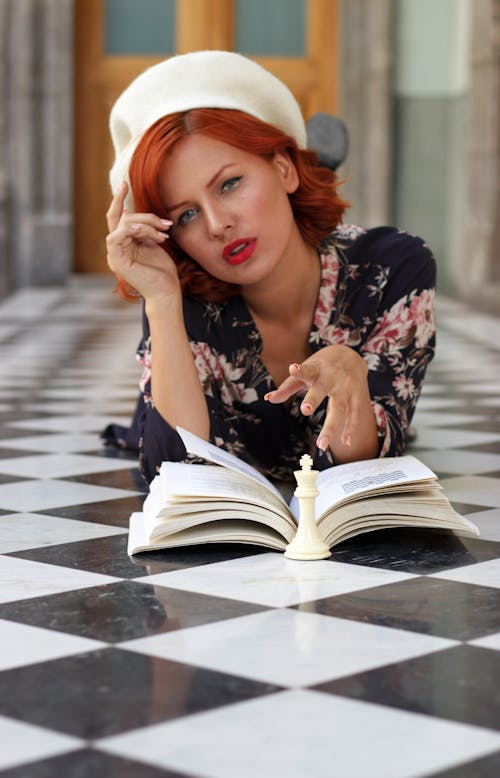 A woman with red hair is laying on the floor with a book