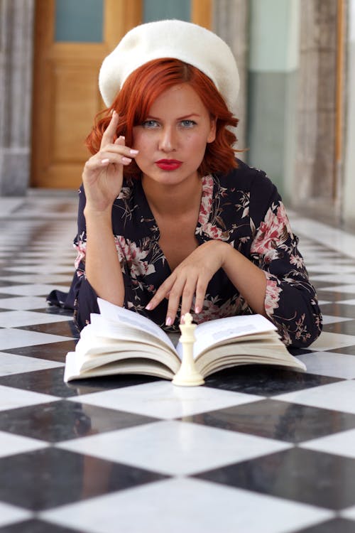 A woman with red hair and a hat is reading a book