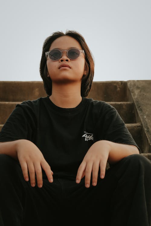 A young man wearing sunglasses sitting on some steps