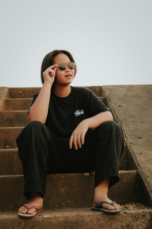 A young woman sitting on some steps wearing sunglasses