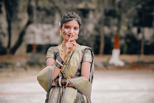 A young woman poses with elegance in a traditional Indian saree, showcasing cultural jewelry outdoors.
