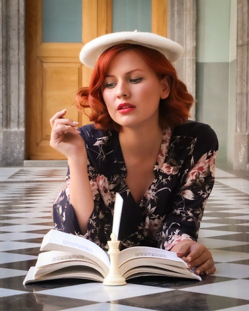 A woman with red hair and a hat reading a book