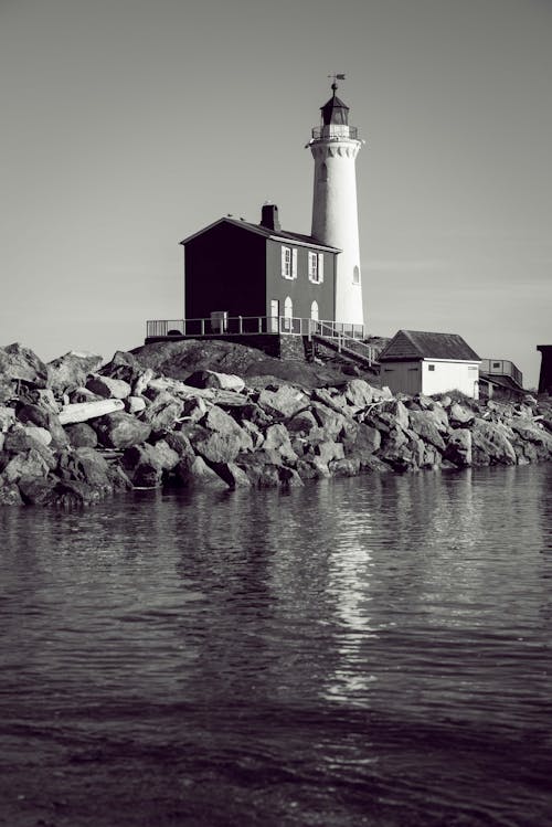 Grayscale Photo Of Lighthouse Tower Beside Body Pf Water