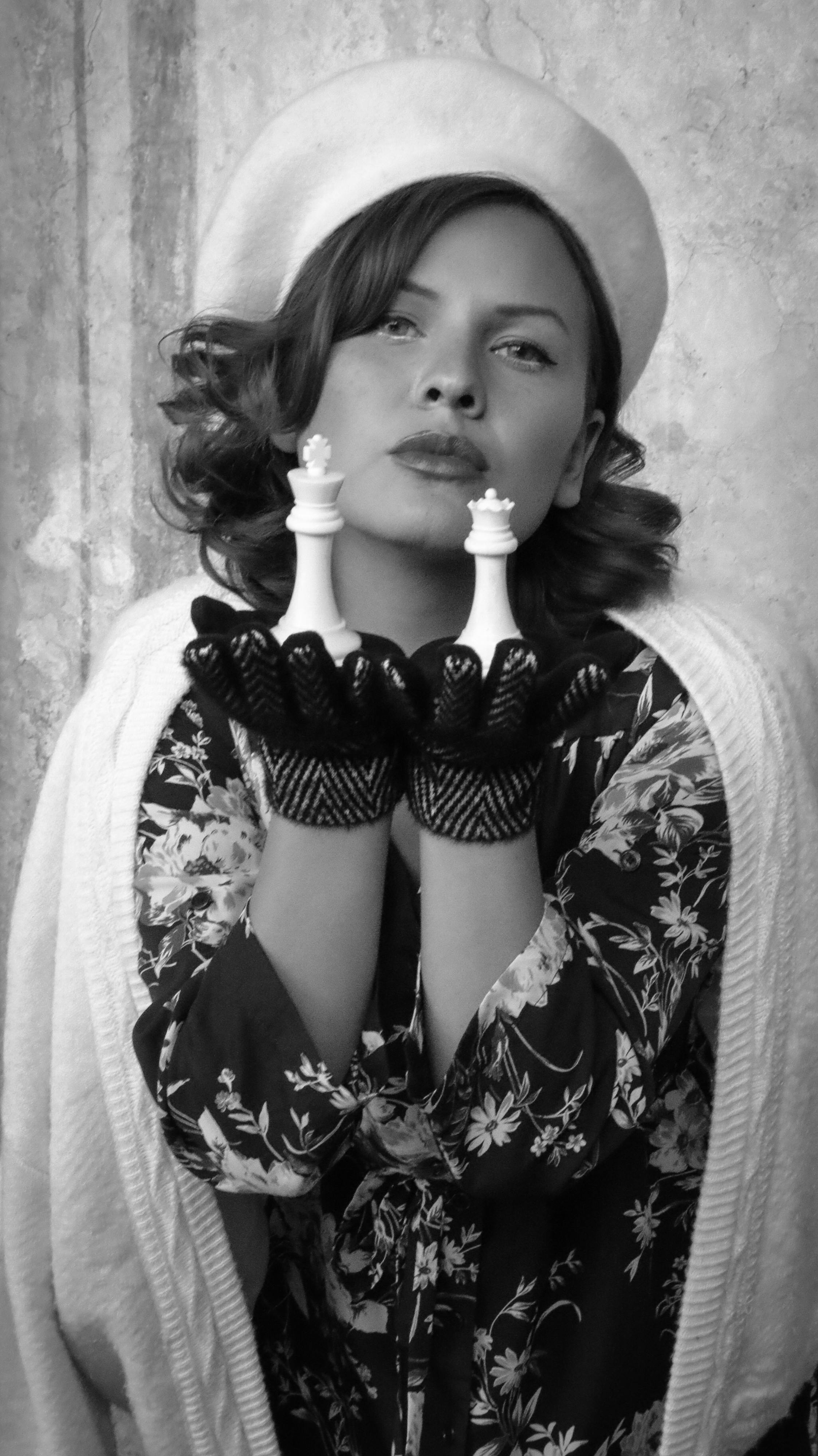 A stylish woman in a beret and gloves holds chess pieces, captured in black and white fashion photography.