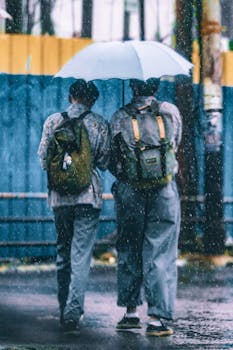 Two individuals navigate a rainy street in Jakarta with an umbrella, showcasing urban life.