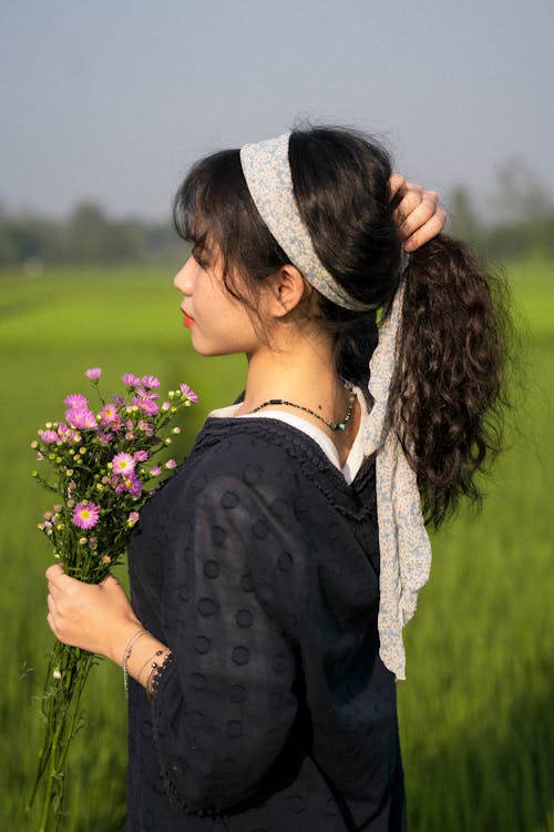 Woman Standing in Field Holding Bouquet of Pink Flowers