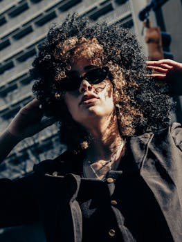 Fashionable woman with curly hair and sunglasses posing in urban Atlanta.