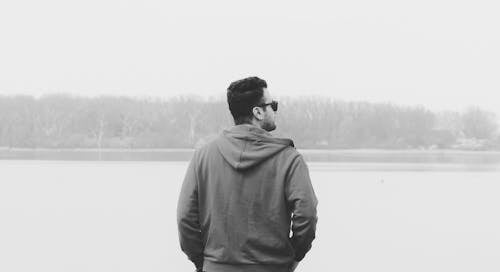 Black and White Photo of Man Standing on Lake Shore