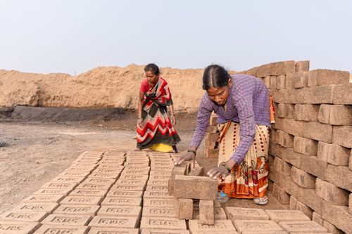 Free Two women arranging bricks in dusty rural area, emphasizing labor and traditional attire. Stock Photo