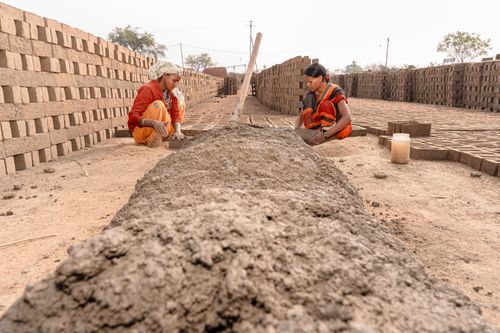 Free Two women working in a sunlit rural brickmaking yard, focused on creating bricks. Stock Photo