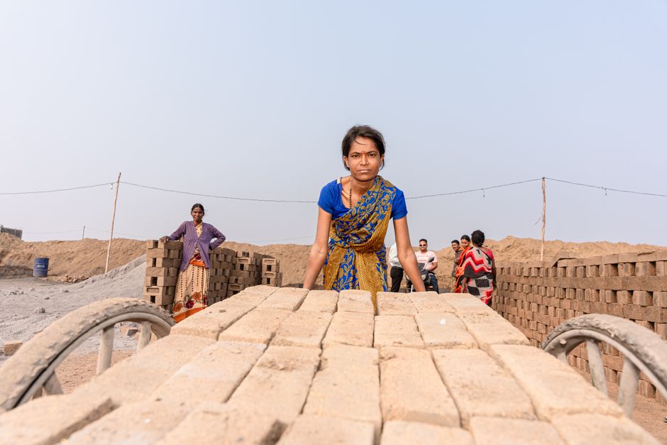 A group of workers in traditional attire, transporting bricks at a rural worksite. Captured in India.