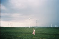 Woman Standing in a Field and Waving with Wind Turbines in the Background