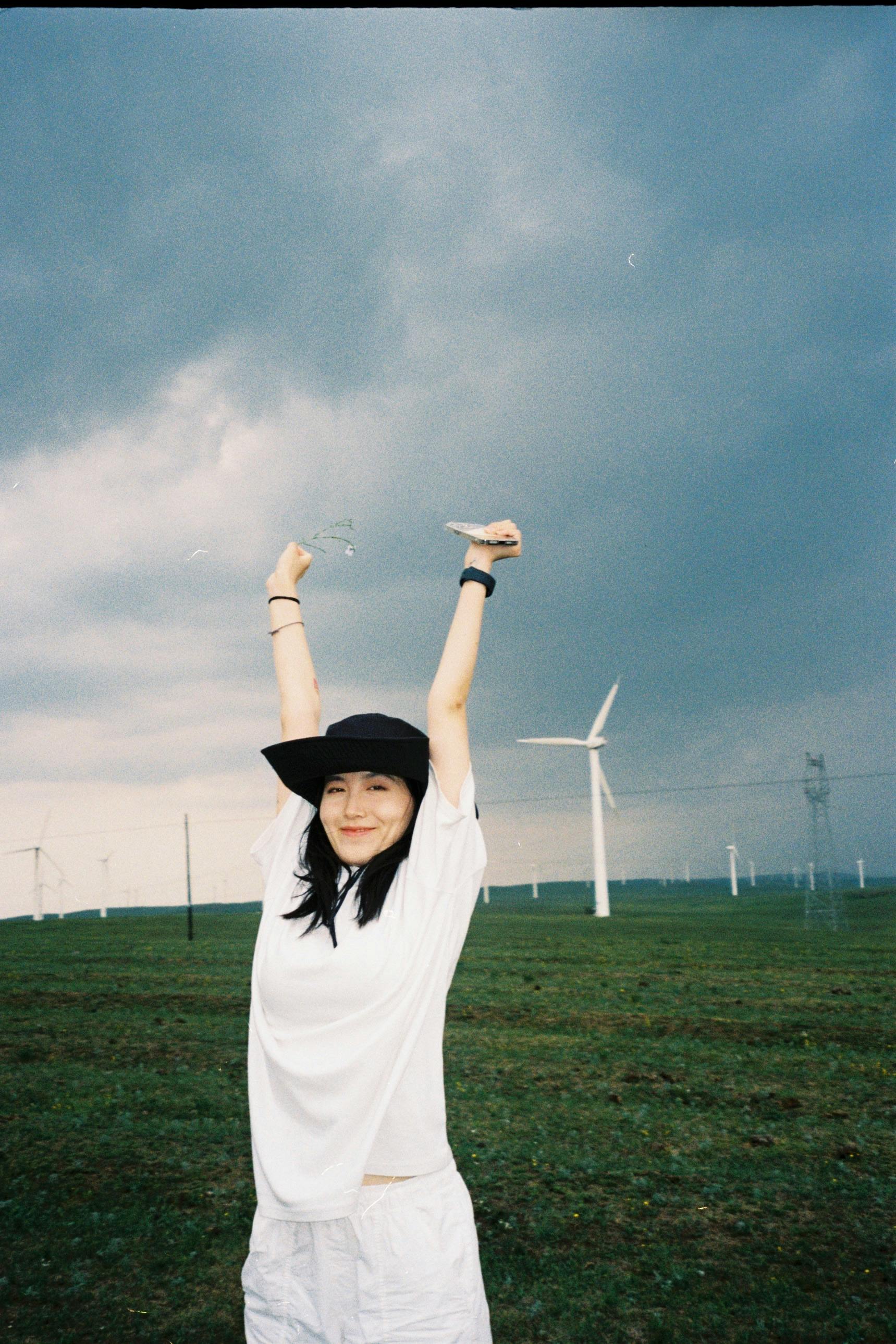 A woman joyfully poses with wind turbines in a rural field in Inner Mongolia, China.