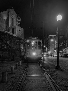 Black and white nighttime view of a tram in Porto, Portugal, showcasing historic urban architecture.