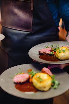 Close-up of gourmet beef meal being served on elegant plates, highlighting detail and presentation.