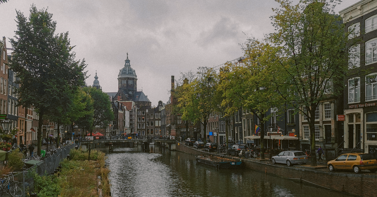 Scenic view of Amsterdam's canal with historic buildings and cathedral on a cloudy day.