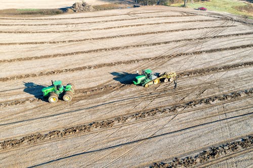 Two Green Tractors Driving on a Cropland