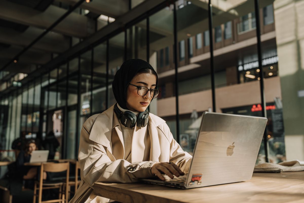 Woman wearing a headscarf sitting in a coworking space with a laptop