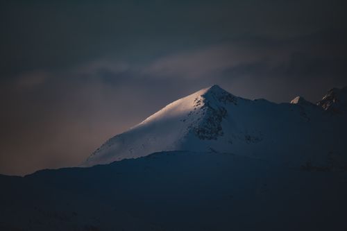 Free A snow-covered mountain peak illuminated by warm twilight lighting, creating a dramatic winter scene. Stock Photo